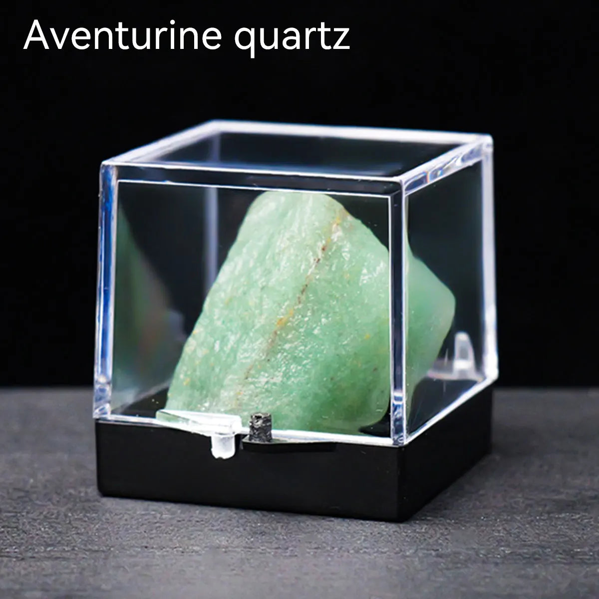A clear display box holds a green aventurine quartz crystal specimen on a dark surface.