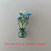 A small glass vase holds a cluster of blue and white flowers for fridge decor.