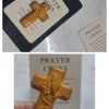 A handcrafted wooden prayer cross with a relief of a praying hand, displayed on a card.