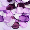 A collection of silk rose petals in shades of purple and pink scattered on a white surface.