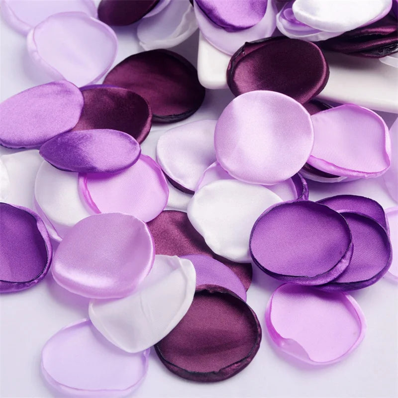 A collection of silk rose petals in shades of purple and pink scattered on a white surface.