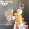 A hand holds a yellow tube of Cereals next to a pink flower magnet on a refrigerator.