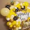 A balloon arch wreath featuring yellow, white, and gold balloons with a honeycomb background for a bee-themed party.