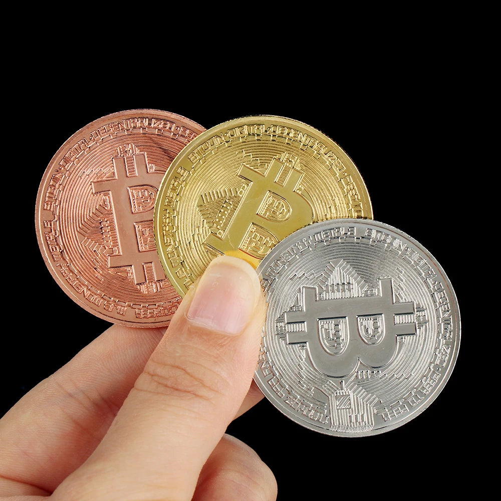 Una mano sostiene tres monedas conmemorativas de Bitcoin: rosa, oro y plata.