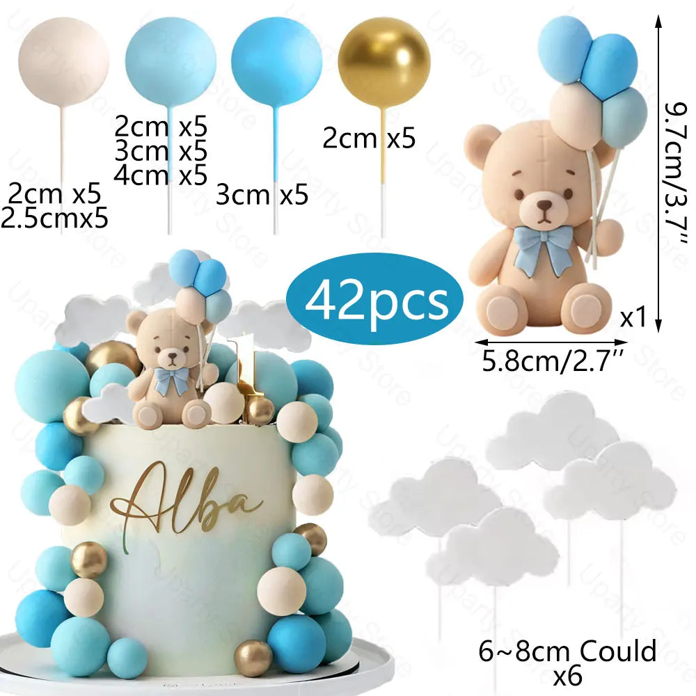 A cake decorated with blue and gold foam balls and a bear topper, accompanied by balloon toppers.