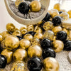 A collection of black and gold confetti balloons is displayed in a woven basket.