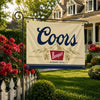A beige flag banner with the word Coors in dark blue script and a mountain graphic, displayed on a metal pole outdoors.