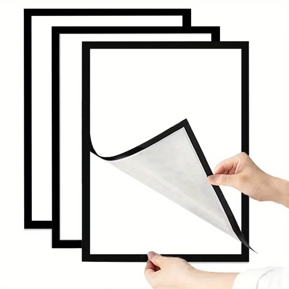 A hand is peeling a white photo from a black magnetic wall frame, showing the minimalist self-adhesive display set.