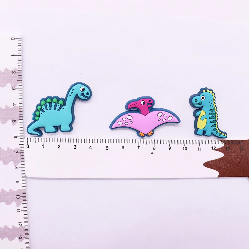 A set of twelve colorful cartoon dinosaur PVC shoe charms displayed next to a ruler.