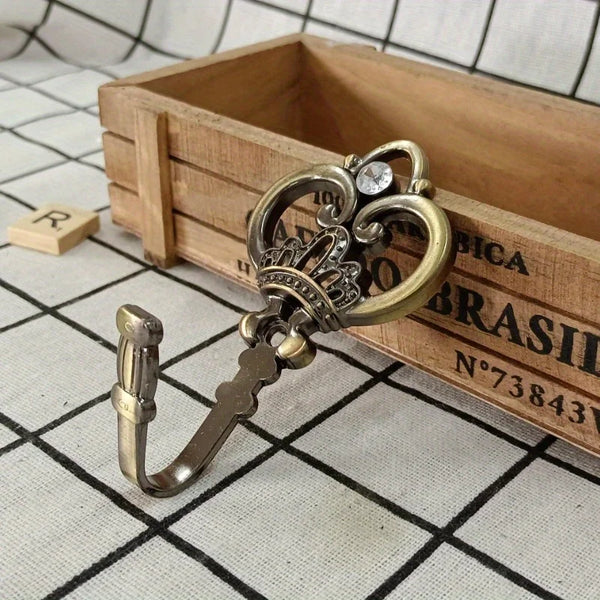 A pair of vintage gold-toned crown curtain hooks resting inside a wooden box with engraved text.