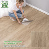 A woman is applying peel and stick wood grain wall tiles to a floor, demonstrating the installation process.