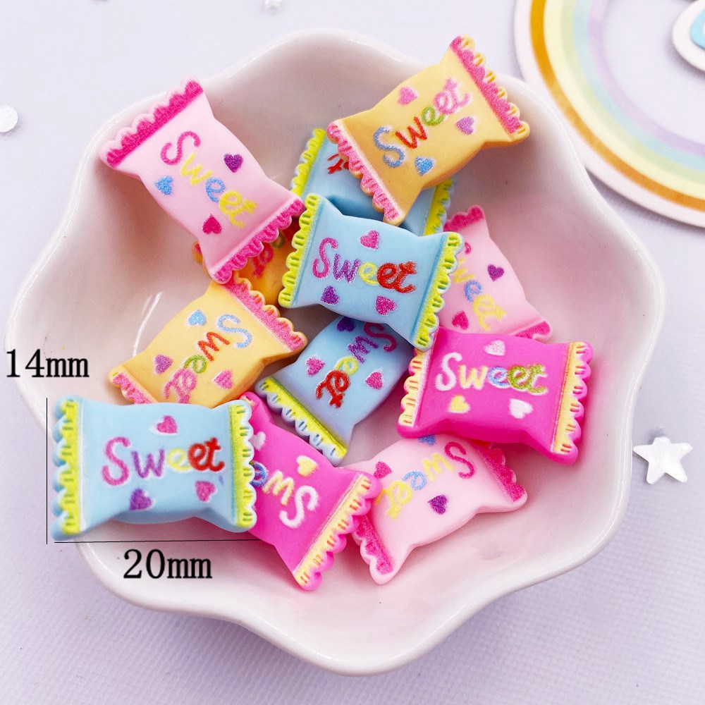 A collection of pink and blue sweet-themed resin candy cabochons for crafting projects displayed in a white bowl.