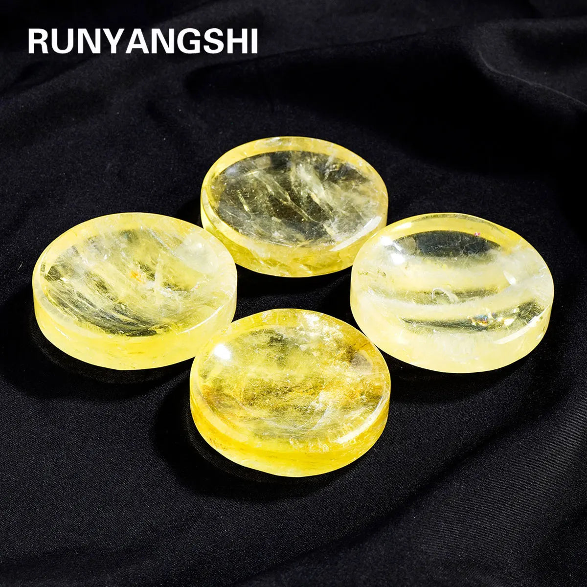 Five smooth, translucent yellow citrine crystals displayed on a black fabric.