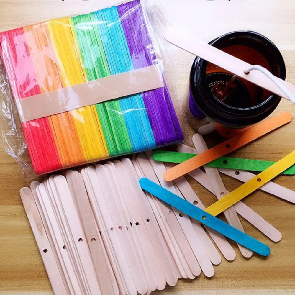 A collection of colorful wooden candle wicks and a glass jar are displayed on a wooden surface.
