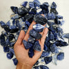 A hand holds a pile of dark blue and white natural raw healing crystal stones for chakra balancing and home decor.