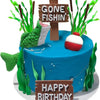 A blue fishing theme party cake decorated with wooden signs and green foliage.