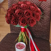 A bouquet of deep red artificial roses with green stems and red ribbon placed on a brown textured surface.