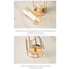 A gold-toned metal and glass candle holder with a removable top, displayed on a light surface.