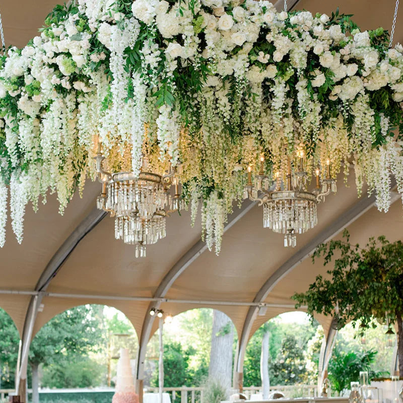 An overhead chandelier made of artificial white wisteria flower garlands hanging inside a tent structure.