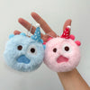 A hand holds two fluffy blue and pink plush doll keychain charms with conical ears