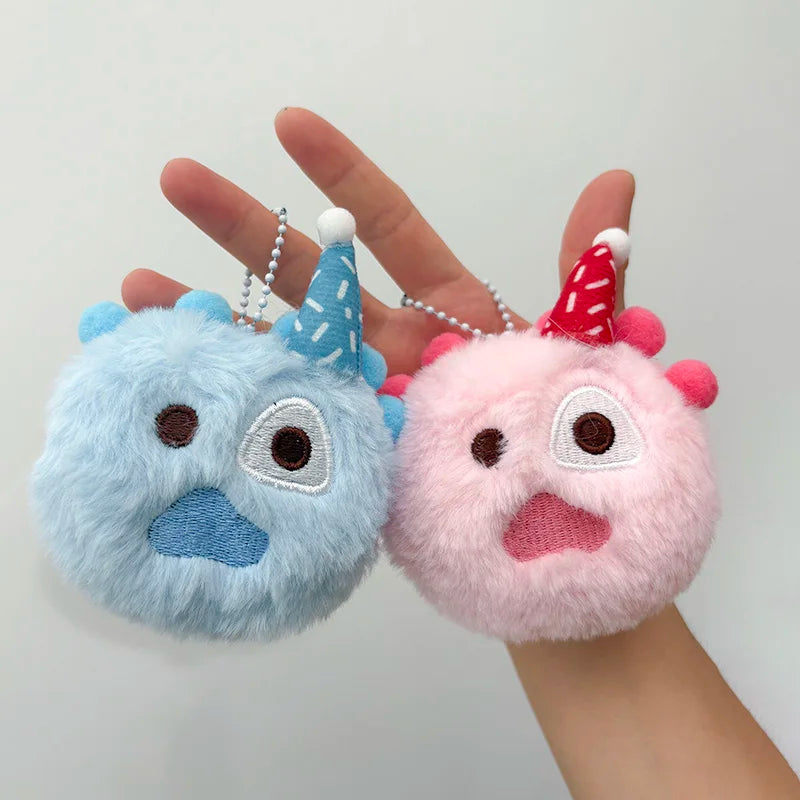 A hand holds two fluffy blue and pink plush doll keychain charms with conical ears