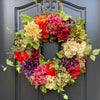 Artificial hydrangea wreath featuring mixed flowers in shades of red, pink, purple, and yellow, displayed on a dark door.