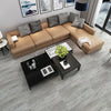 A modern living room featuring a tan sectional sofa, decorative pillows, and black coffee tables on a gray wood-look floor.