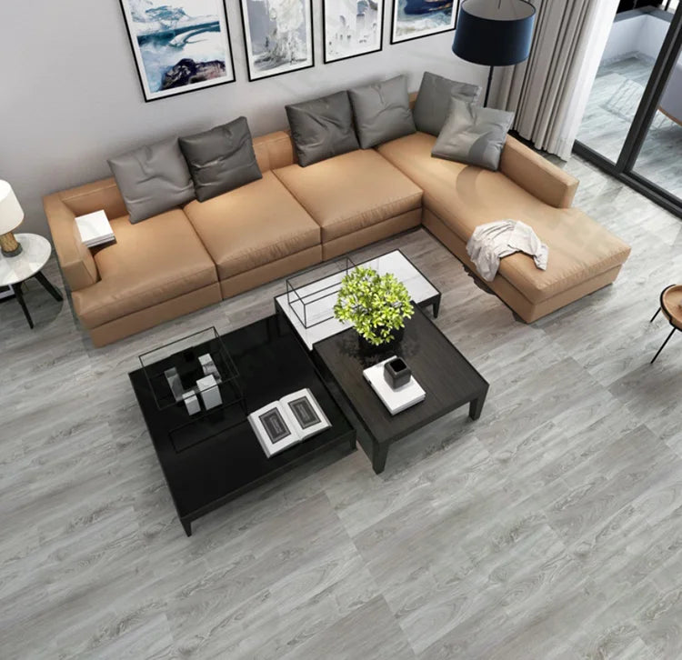 A modern living room featuring a tan sectional sofa, decorative pillows, and black coffee tables on a gray wood-look floor.