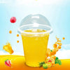 A glass of orange juice in a clear plastic cup with a dome lid surrounded by citrus fruits and a strawberry.