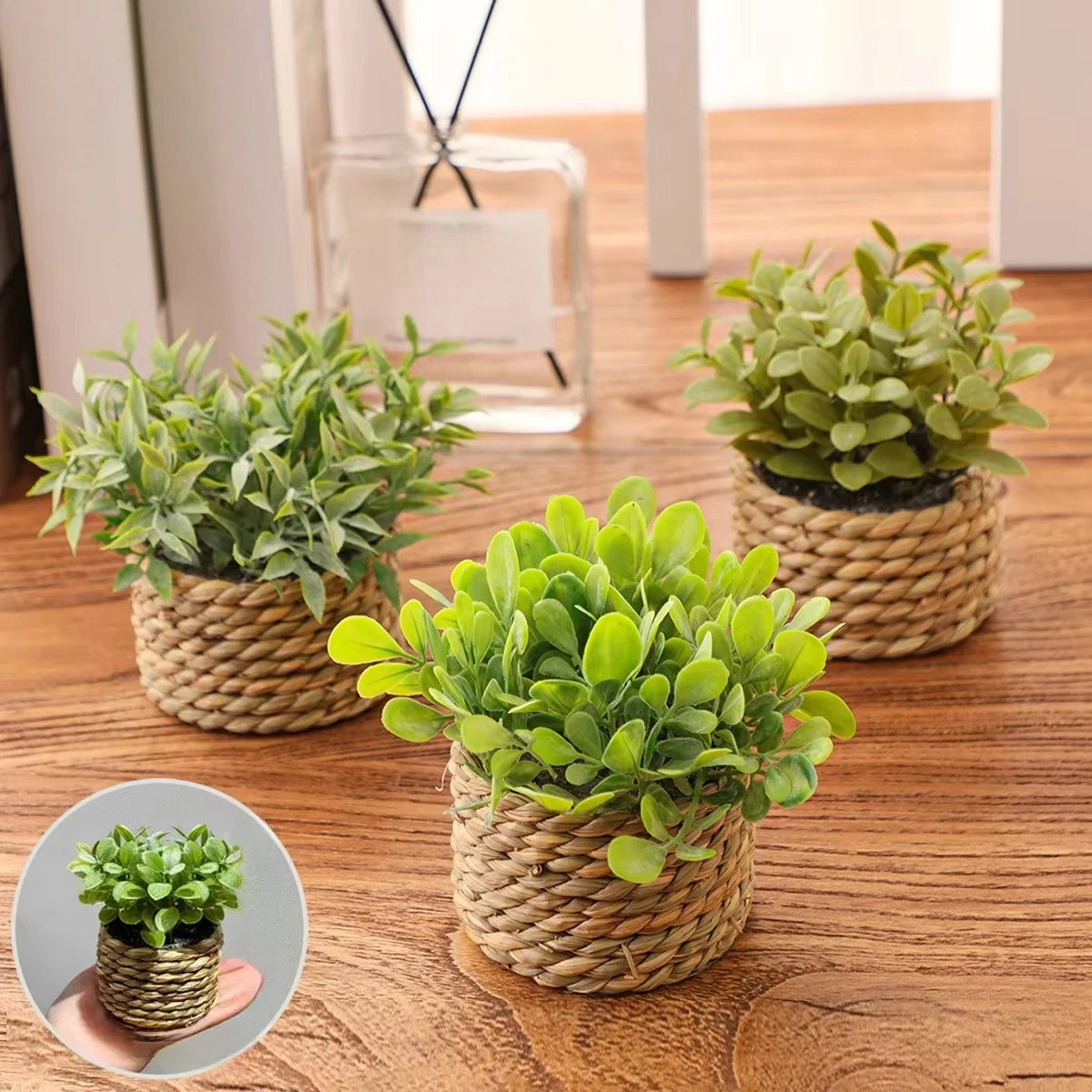 A potted artificial plant with green leaves sits on a wooden surface.
