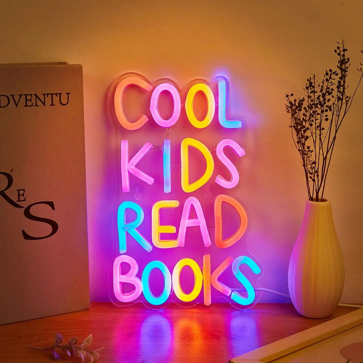 A neon sign spelling out COOL KIDS READ BOOKS illuminated on a wall.