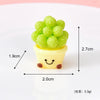 A small yellow resin charm shaped like a smiling face with green textured balls on top.