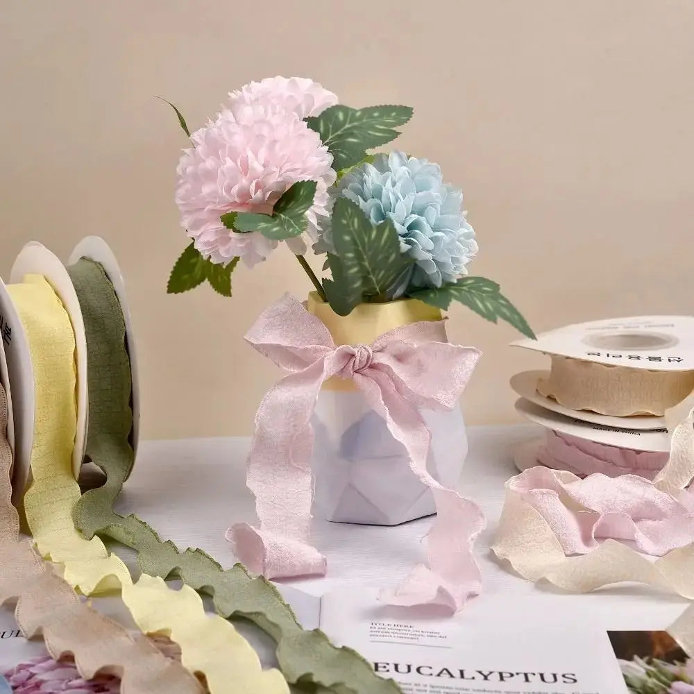 Pink and blue floral yarn ribbon displayed in a white vase with green leaves.