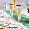 A close-up of clear plastic champagne flutes with gold accents set on a white table with green fabric.