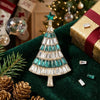 A sparkling rhinestone Christmas tree brooch pin displayed on a dark green velvet fabric with pine cones and festive decorati