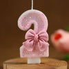 Topper de vela número 9 brillante rosa con lazo rosa sobre una superficie de madera.