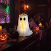 An adjustable glowing ghost light fixture sits on a dark shelf next to carved pumpkin treats.