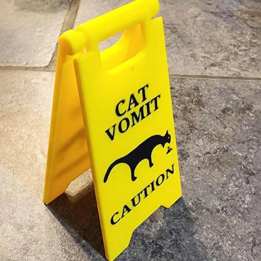 A yellow plastic yard sign with black text warning about cat vomit.