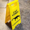 A yellow plastic yard sign with black text warning about cat vomit.