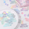 Holographic disco confetti scattered on a white plate and surrounding surface.