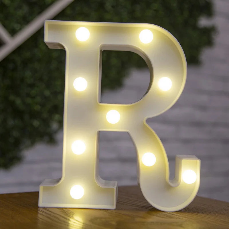 A glowing warm white LED alphabet letter light shaped like the letter R, resting on a wooden surface.
