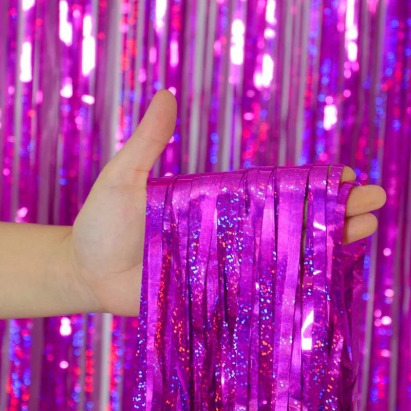 A hand holds a vibrant purple metallic foil tinsel fringe backdrop set against a sparkly curtain background.