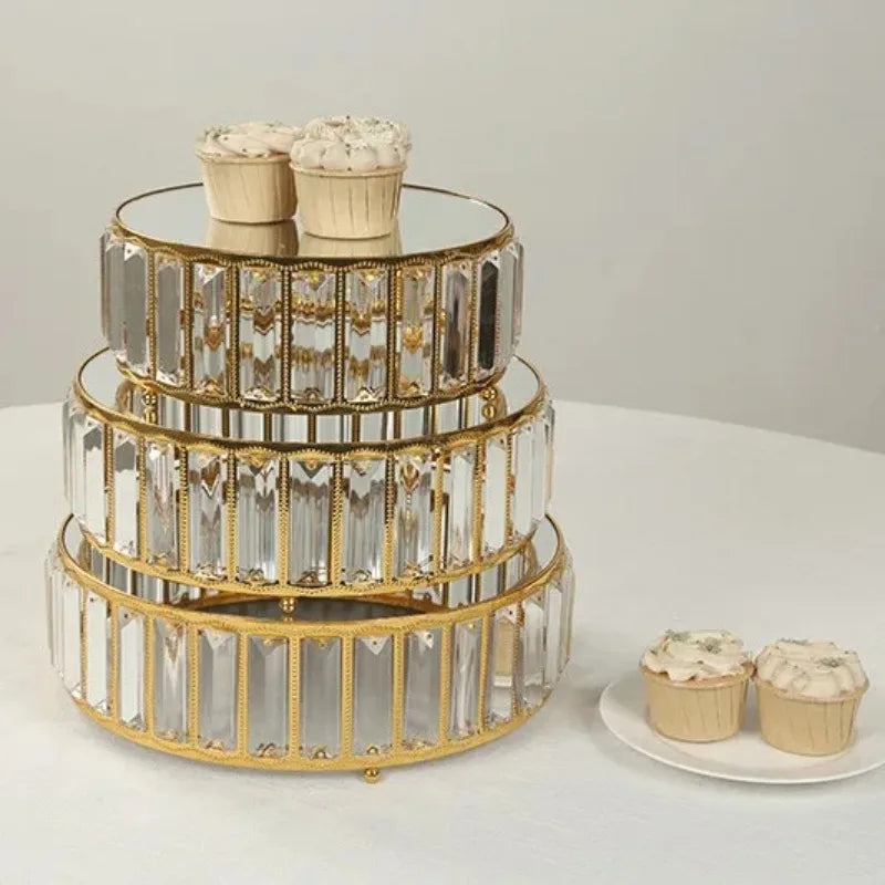 A set of three clear crystal and gold metal tiered cake stands displaying cupcakes.