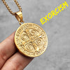 A gold-toned stainless steel punk cross necklace hanging from a chain, held by a hand.