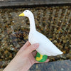 A white garden statue of a goose with yellow accents is held above a bed of small stones.