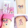 A collection of colorful glitter unicorn temporary tattoos on a skin, next to the packaging.