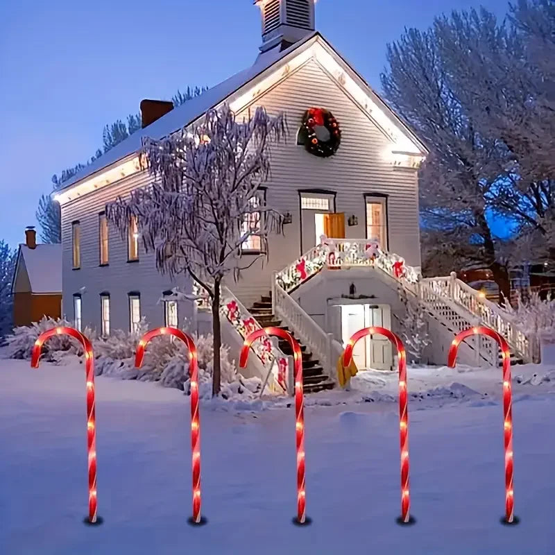 Five red and white candy cane pathway lights illuminate a snowy outdoor scene in front of a house.