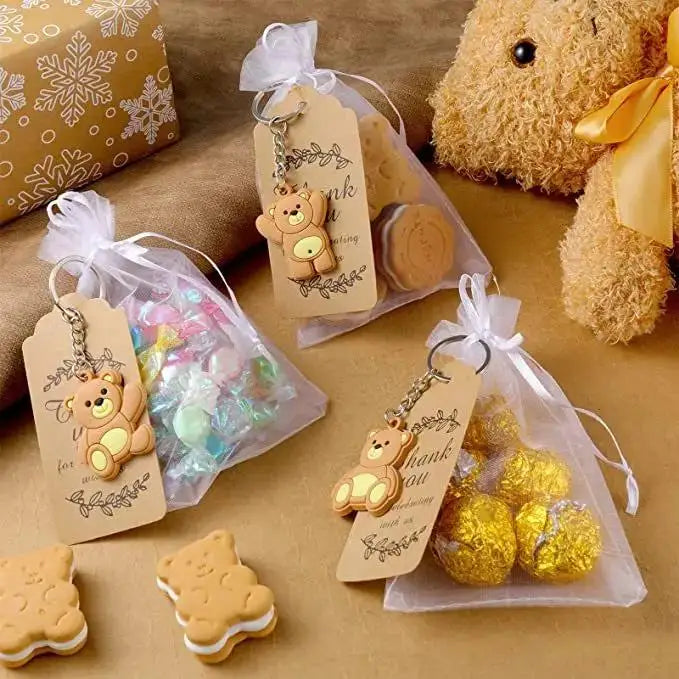 A collection of cute bear keychains and party favors packaged in organza bags with thank you tags on a brown surface.