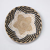 A round woven straw wall decor hanging featuring concentric black and white stripes.