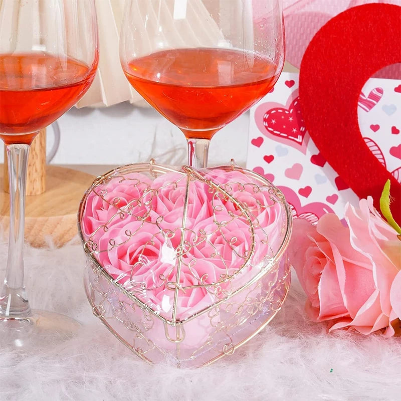 Una copa de vino tinto se encuentra detrás de un recipiente transparente en forma de corazón lleno de rosas artificiales rosa